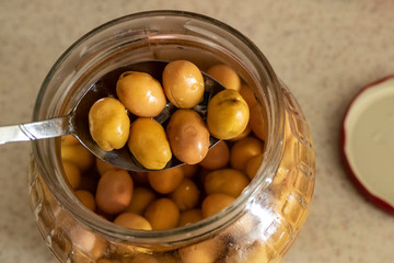 green scratched olives and spoon in jar, close-up,
