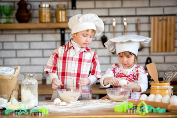 Children a boy and a girl prepare delicious gingerbread and cookies in the kitchen from flour and eggs