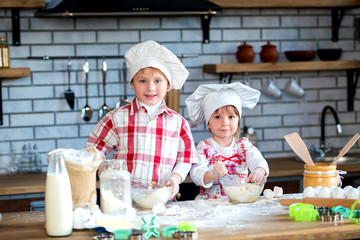 Children a boy and a girl knead a dough of flour and eggs and prepare delicious gingerbread and...