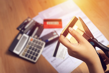 women use scissors to cut credit cards in hand with many credit card and statement on table for...