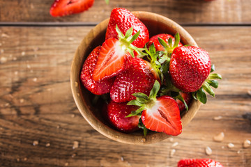 Juicy washed strawberries in wooden bowl on kitchen table