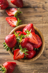 Juicy washed strawberries in wooden bowl on kitchen table