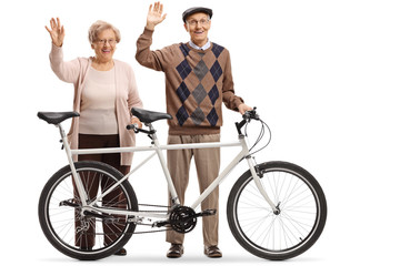 Obraz premium Elderly couple of a man and woman with a tandem bicycle waving
