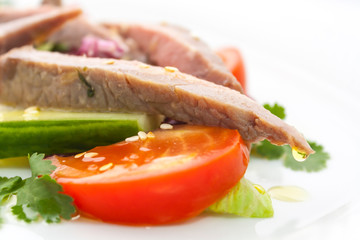 a drop of clear olive oil hangs on the tip of a piece of ham in a vegetable salad of meat and vegetables