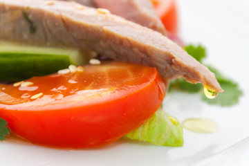 parsley is reflected in a drop of clear olive oil, which hangs on the tip of a piece of ham next to a red tomato in a vegetable salad of meat and vegetables