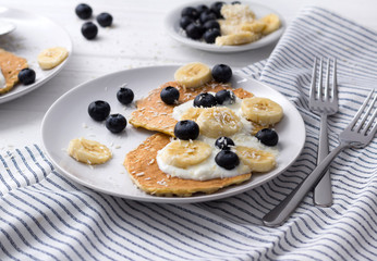 Homemade oatmeal pancakes with yogurt, fresh blueberry and banana at white wooden background.