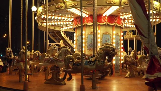 Bright glowing in golden garland carousel with horses slowly rotates at fair at night