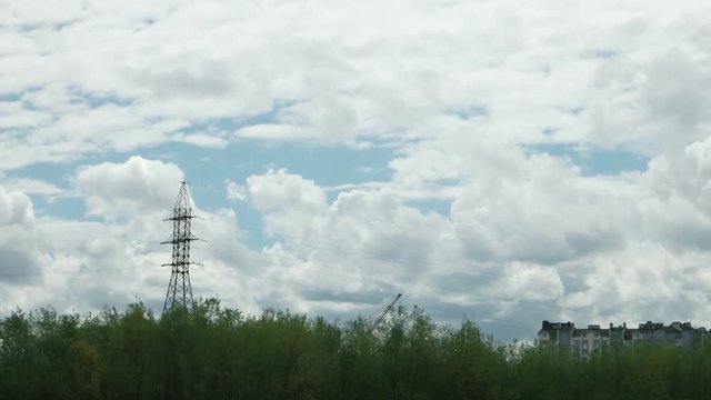 Tower for support of overhead power line against the background of white clouds, moving across the blue sky, time lapse
