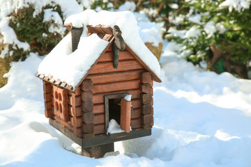 Wooden bird feeder in shape of house on winter day