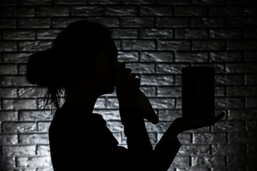 Silhouette of crying woman with mortuary urn on dark brick background