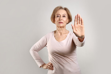 Beautiful mature woman showing stop gesture on grey background