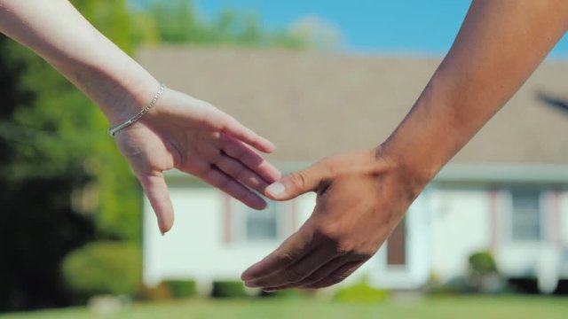 A young couple takes each other's hands against the backdrop of their new dream home. Buying real estate concept