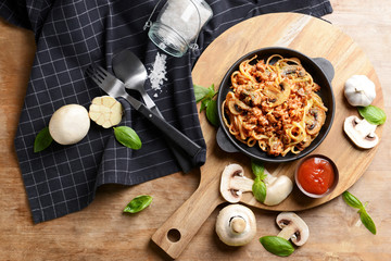 Frying pan with tasty boiled pasta, tomato sauce and mushrooms on wooden table