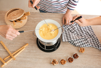 Women eating tasty cheese fondue at table