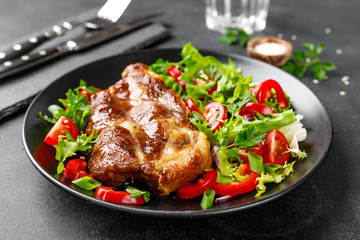 Baked pork steak with fresh vegetable salad on a plate