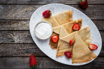 Crepes with strawberry and cream sauce. Homemade thin crepes for breakfast or dessert on wooden background, top view.