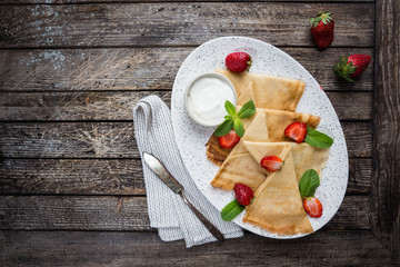 Crepes with strawberry and cream sauce. Homemade thin crepes for breakfast or dessert on wooden background, top view.