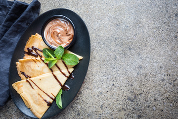 Crepes with chocolate spread. Homemade thin crepes for breakfast or dessert on stone background, top view.