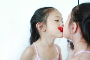 Adorable funny little girl apply lipstick over her mouth near a mirror.
