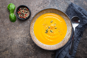 Vegetarian autumn pumpkin cream soup with seeds on dark background, top view