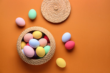 Wicker basket with beautiful Easter eggs on color background