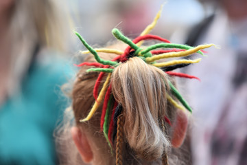Une tête blonde d'enfant qui a une queue de cheval avec accroché des bouts de laines rouge vert...