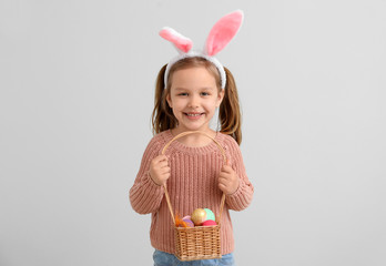 Little girl with Easter eggs and bunny ears on light background