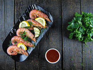 Fototapeta na wymiar Boiled shrimps with lemons, greens and sauce on a wooden background. Top view