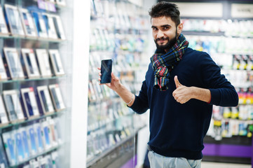 Indian beard man customer buyer at mobile phone store choose his new smartphone and show thumb up. South asian peoples and technologies concept. Cellphone shop.