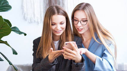 Surprised two young women blogger chatting with best friends in social network on mobile phone while received shocking good news using wifi zone and reading interesting book indoors after work