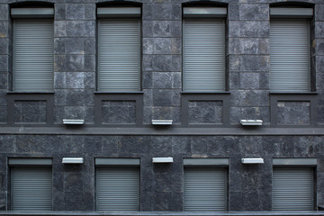 Fototapeta na wymiar Architecture building fasade from grey granite stone with windows closed with metal rollets