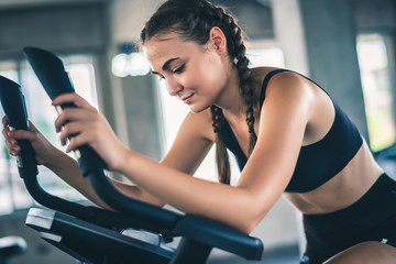 Attractive young woman biking in the gym, exercising legs doing cardio workout cycling bikes.