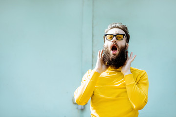 Portrait of a confident stylish bearded man in yellow sweater on the turquoise background outdoors