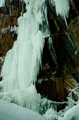 Frozen waterfall among the rocks. The waterfall is freezing, huge icicles. Ice white and blue. Winter waterfall. Russia. Krasnoyarsk Columns is a unique phenomenon.