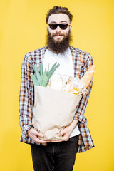 Portrait of a bearded man standing with shopping paper bag full of food on the bright yellow...