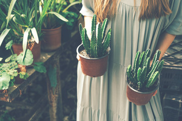 Closeup of a blond woman in a long dress holding 2 pots of succulents in a greenhouse
