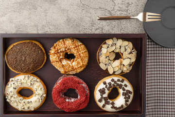 food background of assortment of donuts on wooden tray with dark plate and small fork and napkin