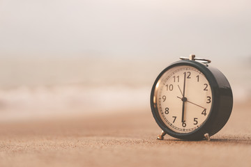 Clock on sand beach with smooth wave background.