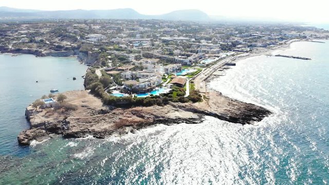 Crete shore build up with luxury resorts and hotels, aerial view from water side. Rocky cape on foreground, developed area perspective, many low rise buildings at Anissaras town
