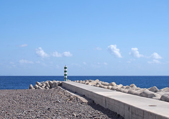 a jetty and breakwater with lighthouse on the beach in funchal madeira with bright sunlit sea and...