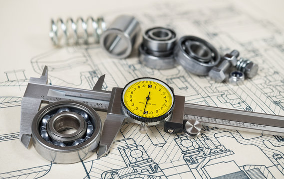 Accurate caliper gauge. Ball bearings diameter. Technical drafting. Analog metal measuring instrument with yellow round dial. Group of steel components on document. Machining concept. Selective focus.