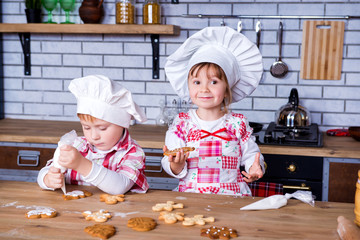 Children a girl and a boy in a cooking chef's hat decorate ready-made baked gingerbread with sweet icing and cream
