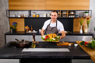Happy man in chef apron demonstrates roasted chicken