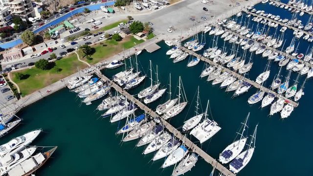Aerial shot of sail yachts parked in shelter, camera fly forward and tilt down. Rows of modern boats stay in marina at Agios Nikolaos city, North-East Crete island area.