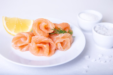 Salted salmon on a white plate with lemon and dill. White background, selective focus, close-up.