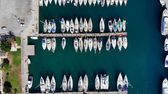 Top view of yacht marina, rows of sailboats parked along jetty, aerial camera fly up. Modern vessels moored at port in Agios Nikolaos, North East coast of Crete Island