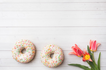 Donuts and flowers tulips on white table with copy space. Flat lay, top view.
