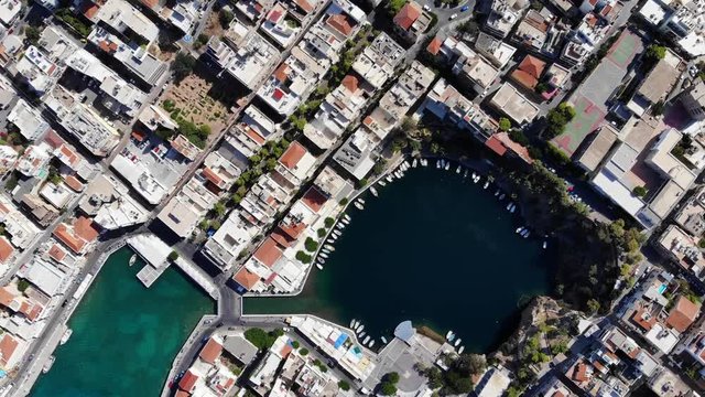Aerial top view shot of Voulismeni lake and Agios Nikolaos city, camera soar over dense build area and small round lake. Popular tourist attraction at Crete Island