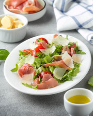 Salad with jamon (parma, ham, serrano, prosciutto), parmesan cheese, lettuce, cherry tomatoes on a plate. Delicious lunch, healthy food, Italian (spanish) cuisine