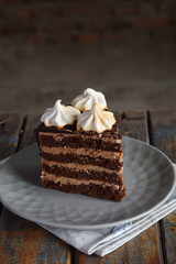 Piece of chocolate cake decorated with rosettes of meringue cream: chocolate-nut biscuit, caramel cream. Homemade baking.